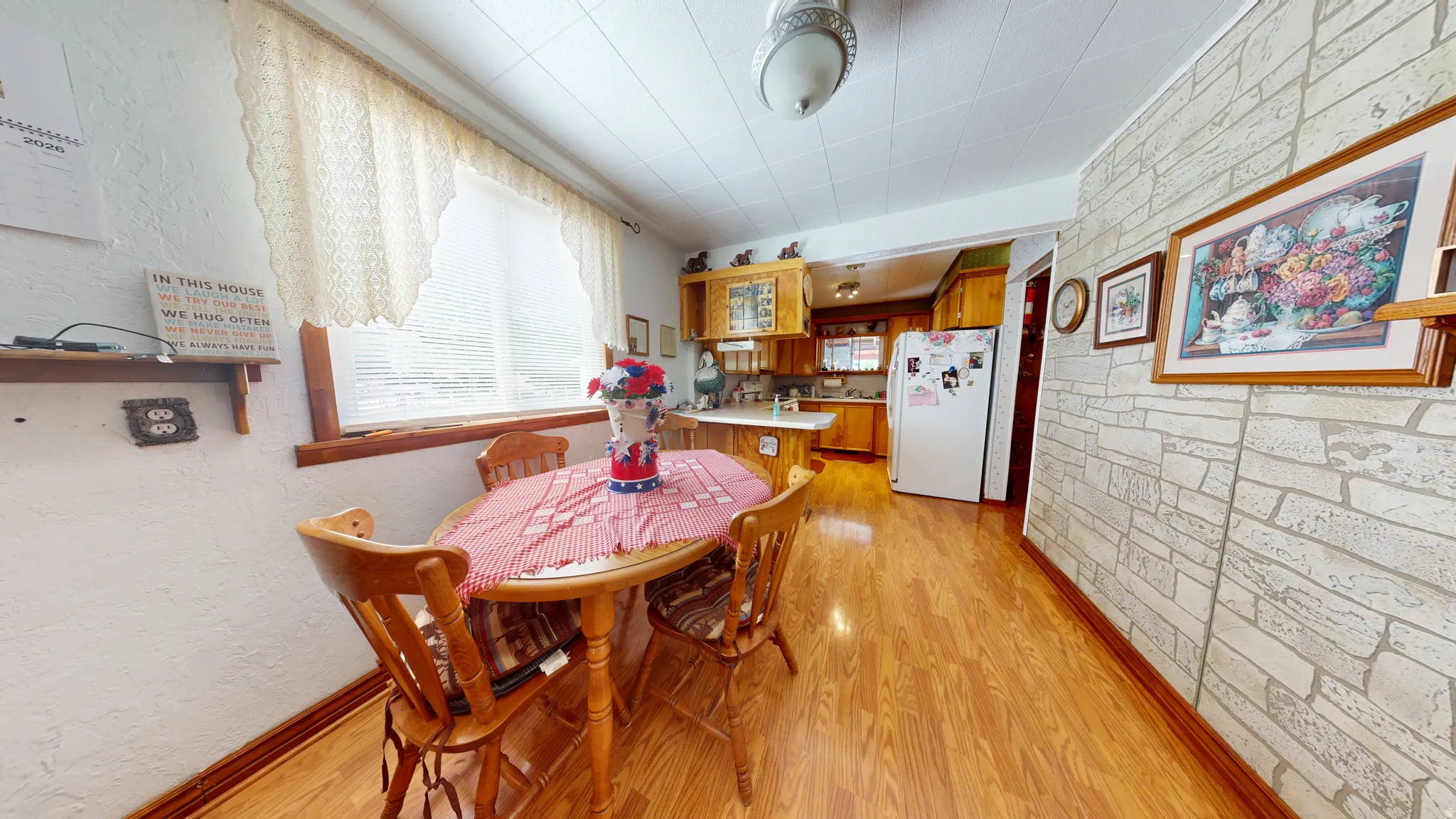 Dining area featuring wood-finish flooring, a window with lace-patterned valance, and a textured stone-pattern wall