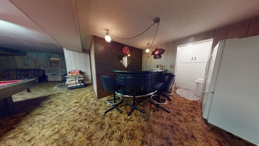 Recreation room featuring a built-in bar with black tufted upholstery, overhead lighting, and wood-paneled walls