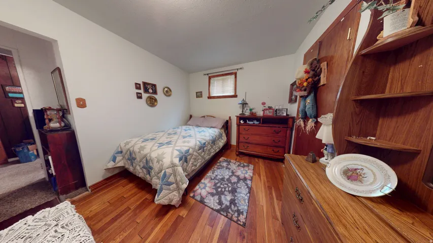 Bedroom featuring rich wood-finish flooring, white painted walls, and a single window with blinds