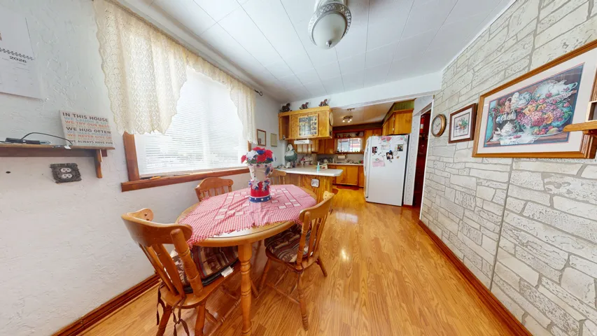 Dining area featuring wood-finish flooring, a window with lace-patterned valance, and a textured stone-pattern wall
