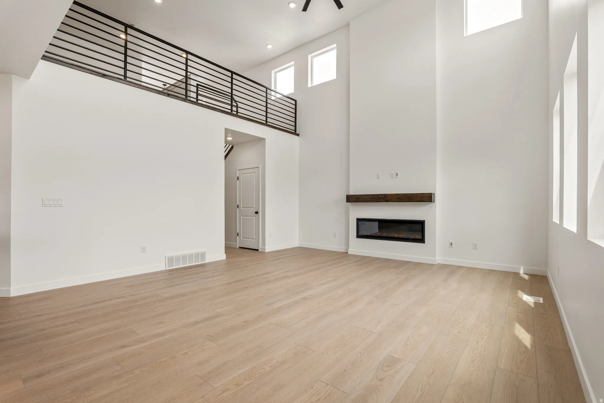 Spacious living area featuring high ceilings, wood-finish flooring, and a modern linear fireplace with a substantial wood mantel
