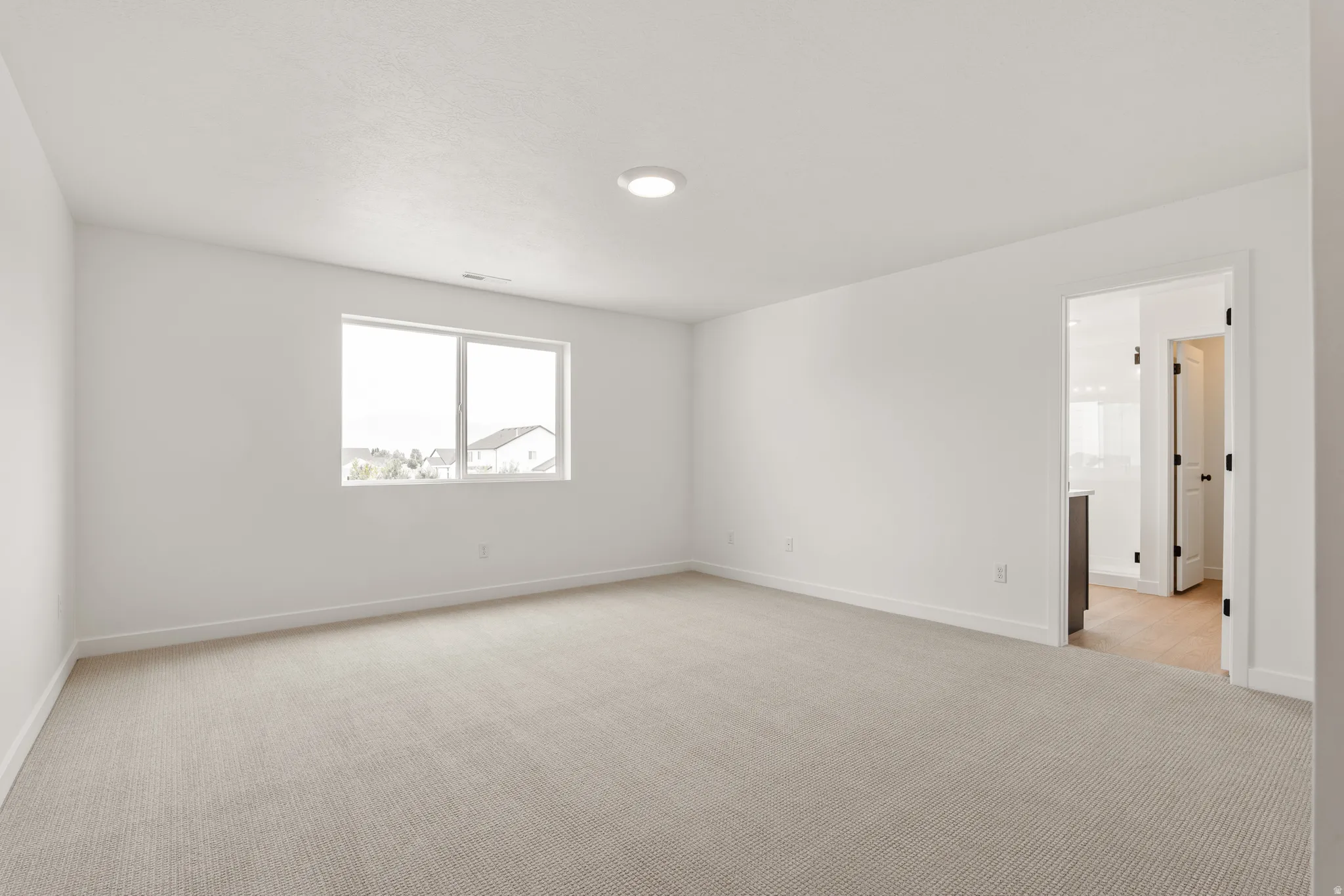 Spacious room featuring neutral carpeting, white walls, and a large window providing ample natural light
