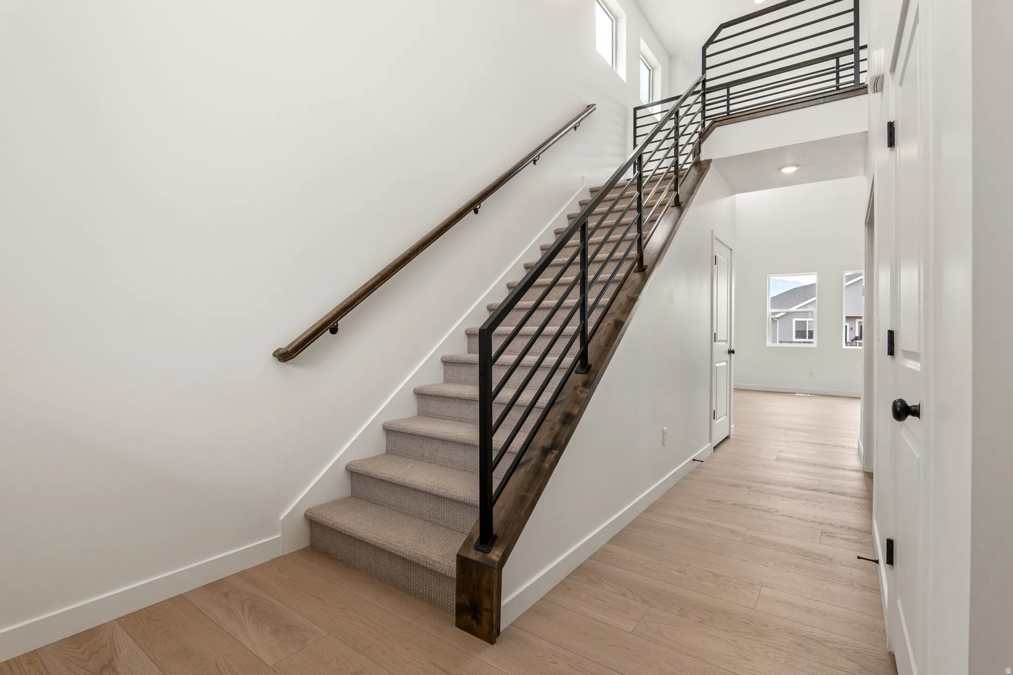 Open foyer featuring a light wood-finish flooring, a contemporary staircase with carpeted treads, dark wood-finish stringers, and a black metal railing