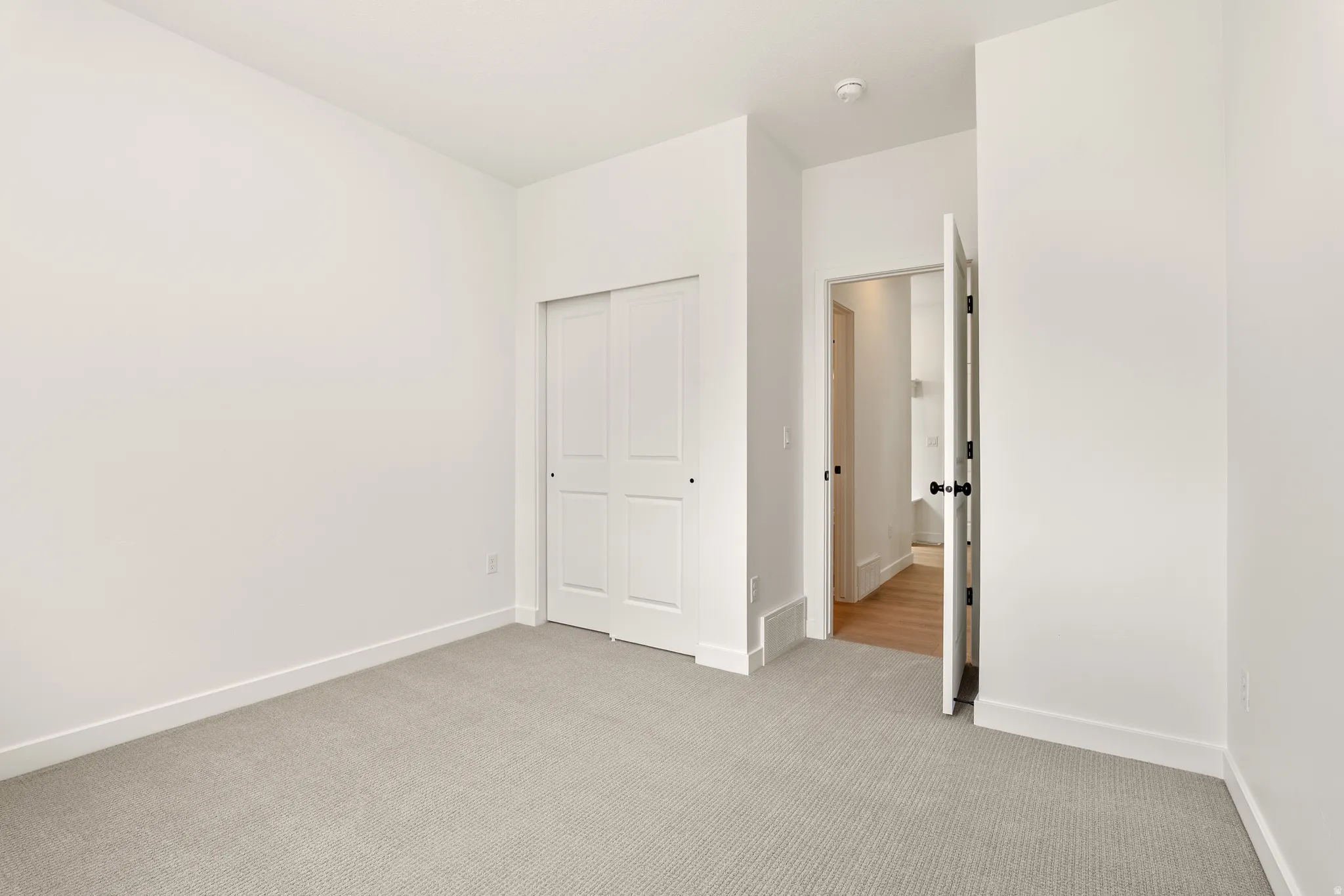 Carpeted room featuring a double bifold closet, white walls, white trim, and a door with a black knob