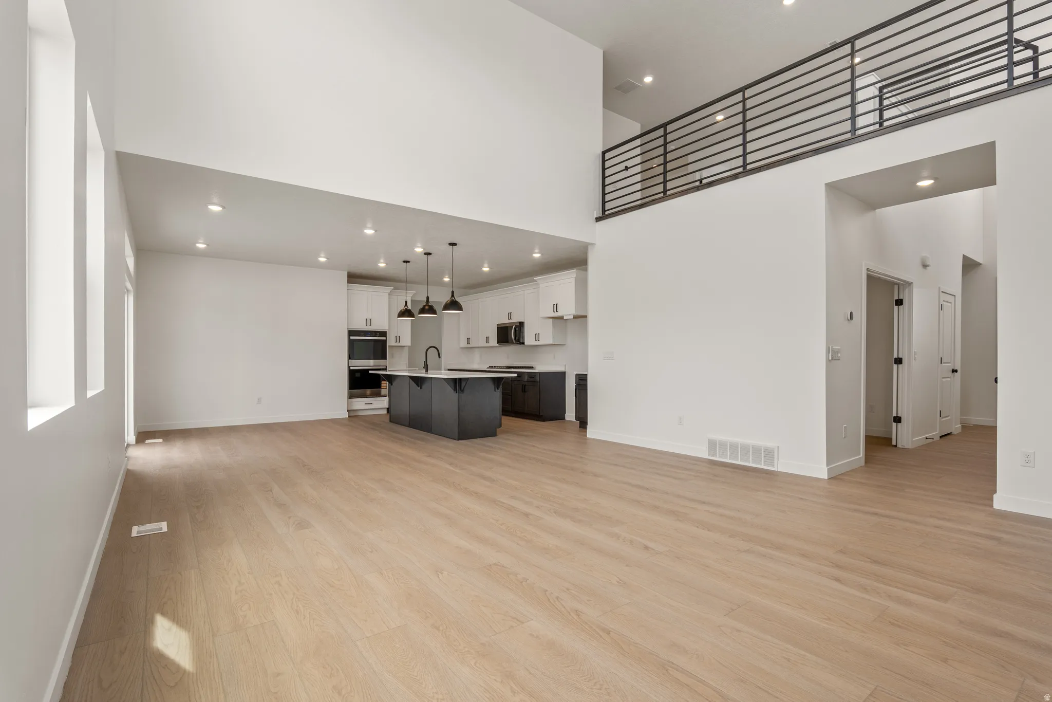 Open-concept living area featuring light wood-finish flooring, high ceilings, and recessed lighting