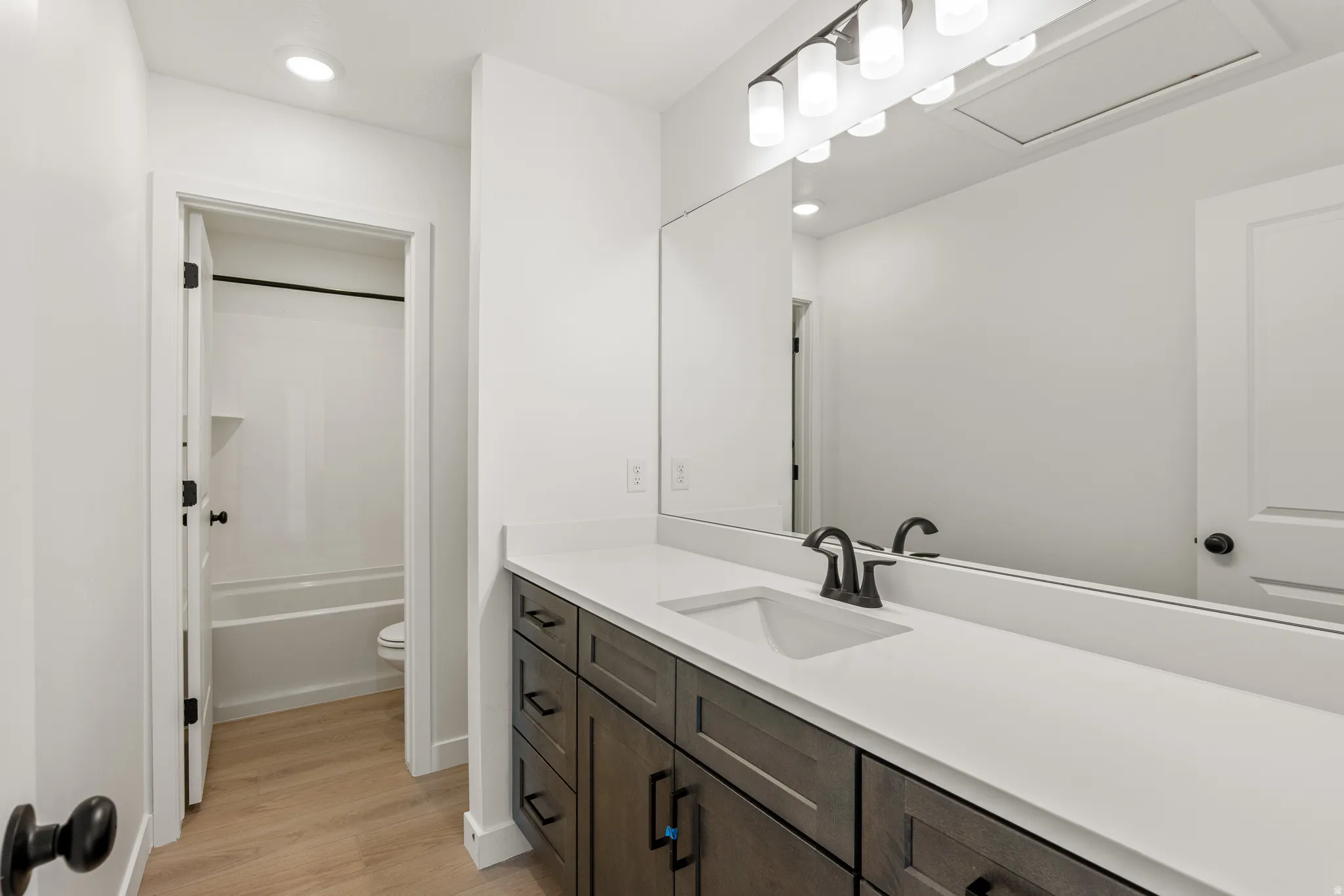 Bathroom vanity featuring an integrated sink with a matte black faucet, a large mirror, and a five-light fixture