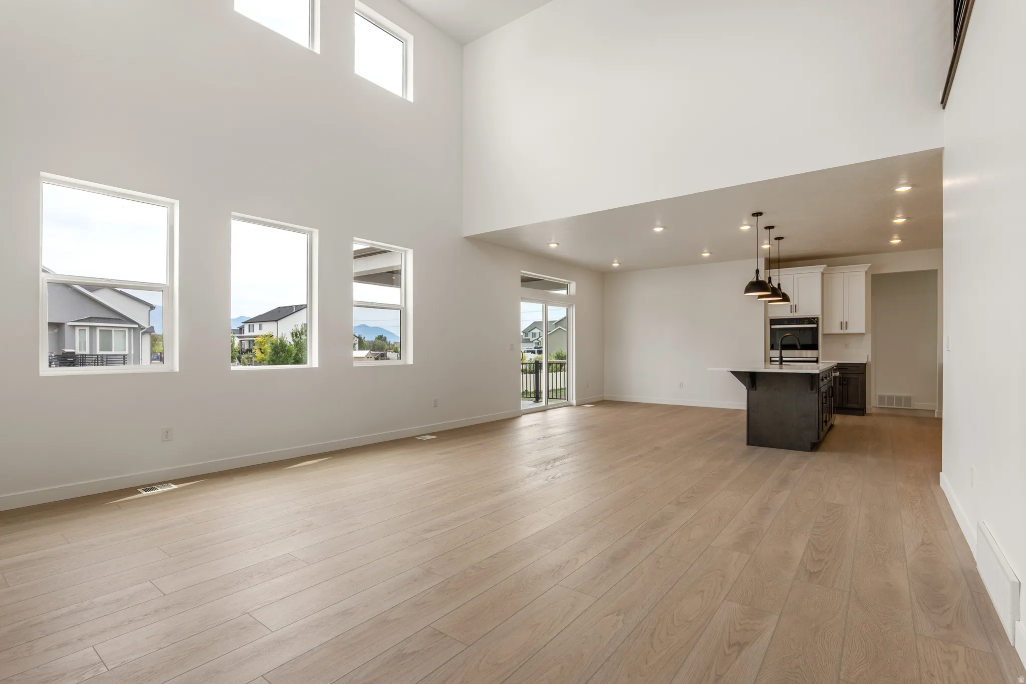 Open-concept living space featuring high ceilings, wood-finish flooring, a modern kitchen island with pendant lighting, a built-in oven, and a sliding glass door to exterior