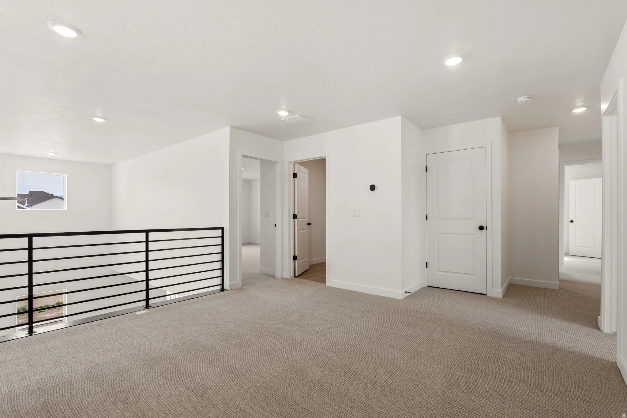 Spacious upper-level landing featuring neutral carpeting, recessed lighting, white interior doors with black hardware, and a modern black horizontal bar railing