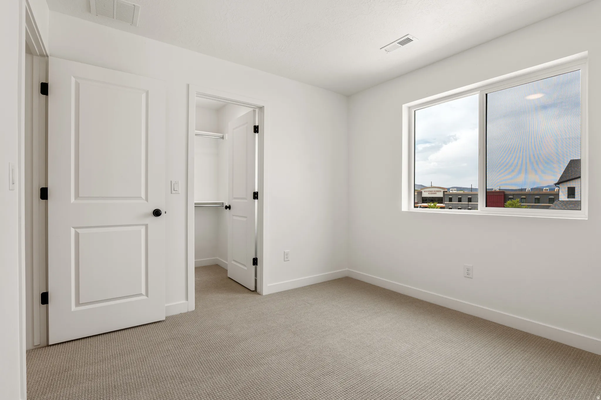 Carpeted room featuring a large window, white trim, and a closet with shelving