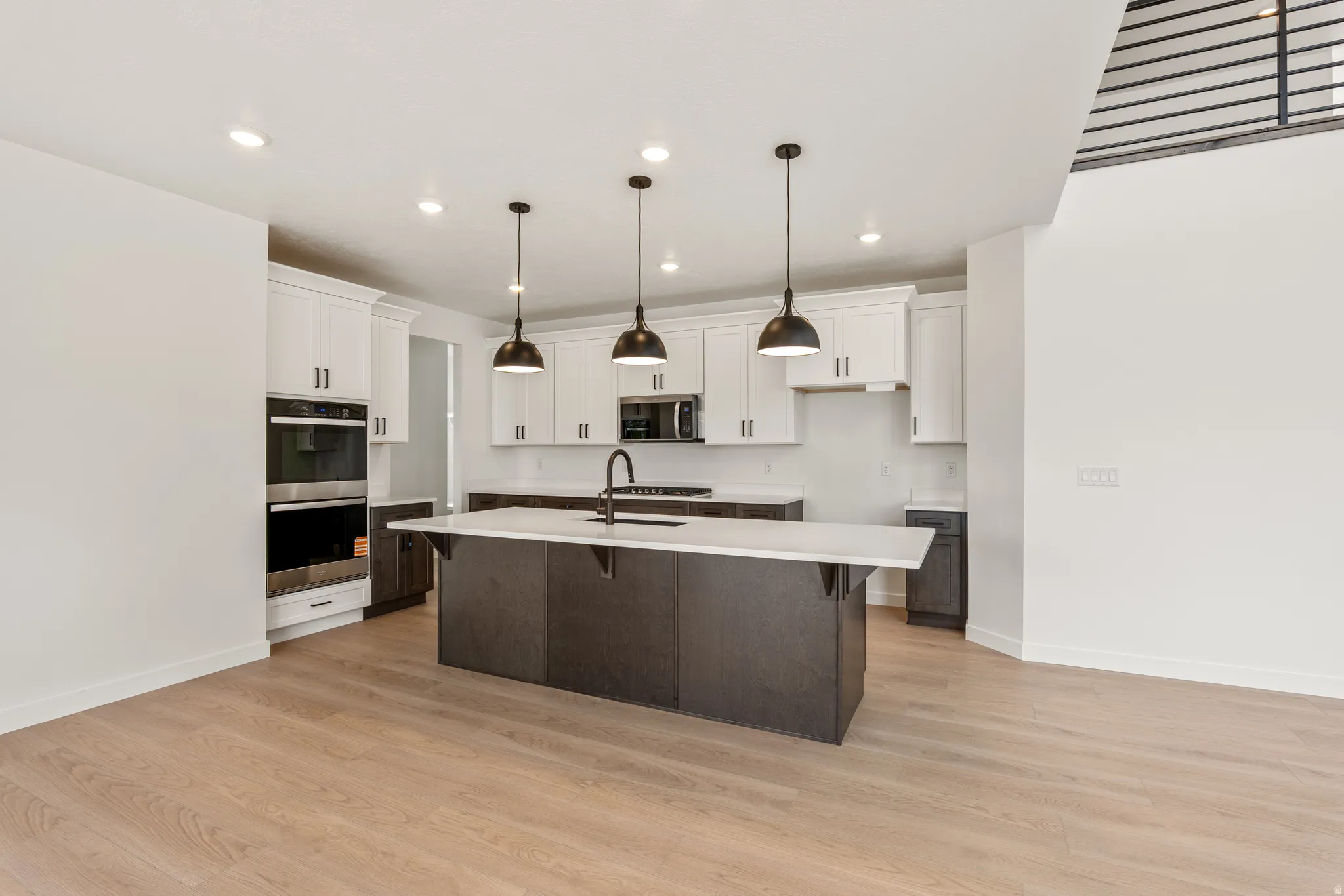 Open-concept kitchen featuring an oversized island with pendant lighting, white upper cabinetry, dark lower cabinetry, light-toned wood-finish flooring, and recessed ceiling lighting