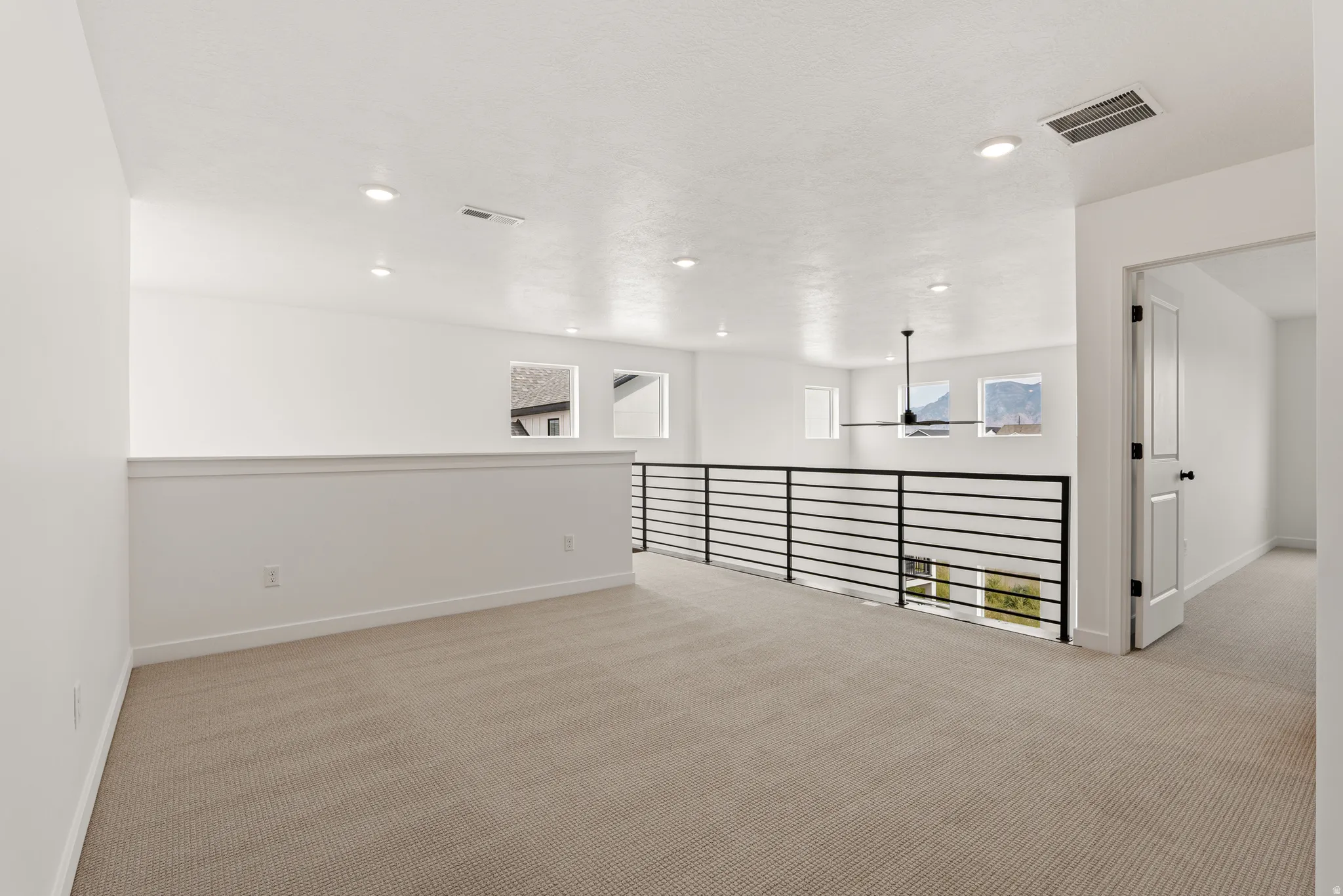 Open loft area featuring neutral carpeting, a modern black horizontal railing, recessed lighting, and a contemporary ceiling fan