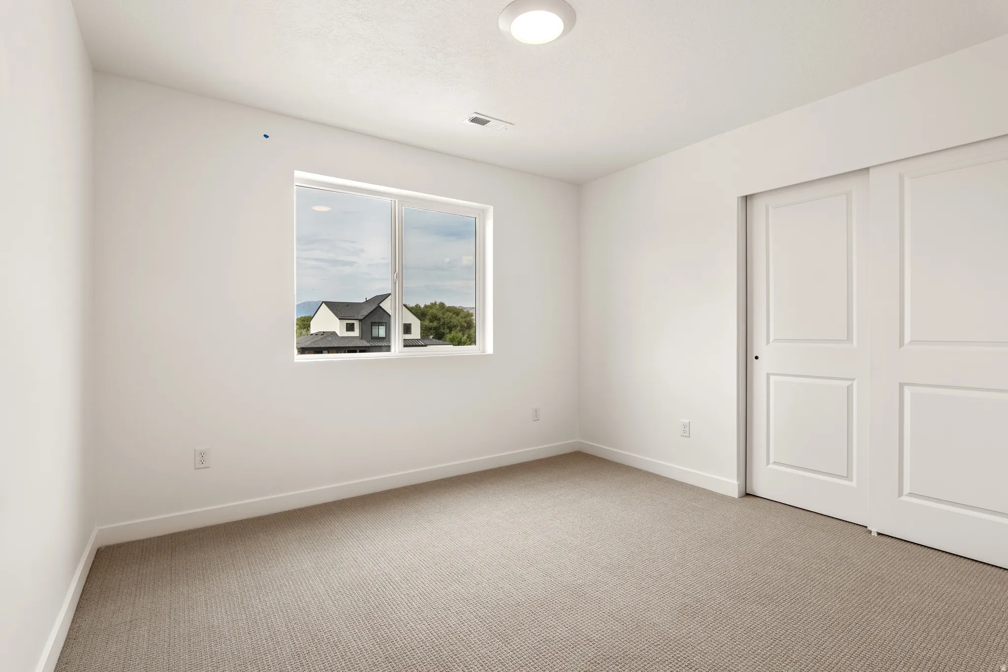Bright room featuring neutral carpeting, white walls, a single window, and a closet with sliding doors