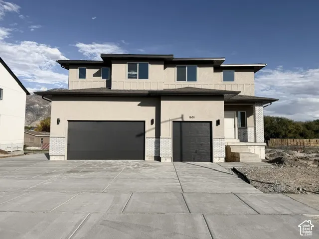 Stucco exterior with brick veneer accents, two attached garages, covered entry, and concrete driveway
