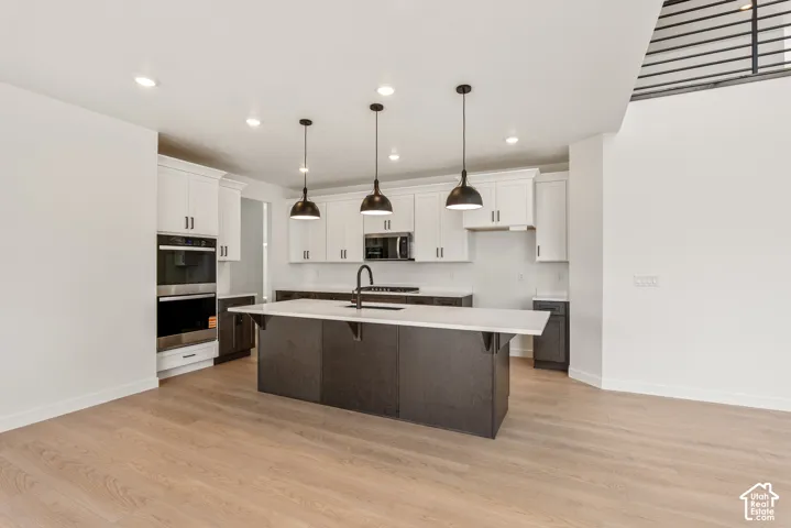 Open-concept kitchen featuring an oversized island with pendant lighting, white upper cabinetry, dark lower cabinetry, light-toned wood-finish flooring, and recessed ceiling lighting