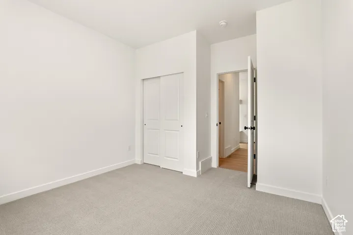 Carpeted room featuring a double bifold closet, white walls, white trim, and a door with a black knob