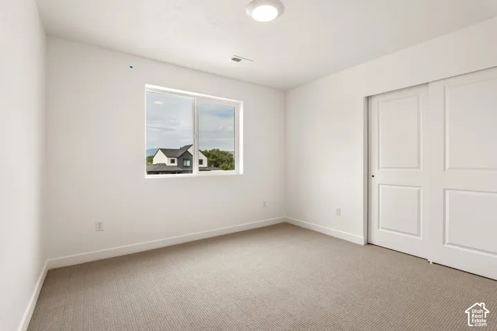 Bright room featuring neutral carpeting, white walls, a single window, and a closet with sliding doors