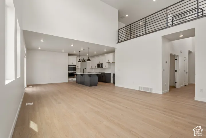 Open-concept living area featuring light wood-finish flooring, high ceilings, and recessed lighting