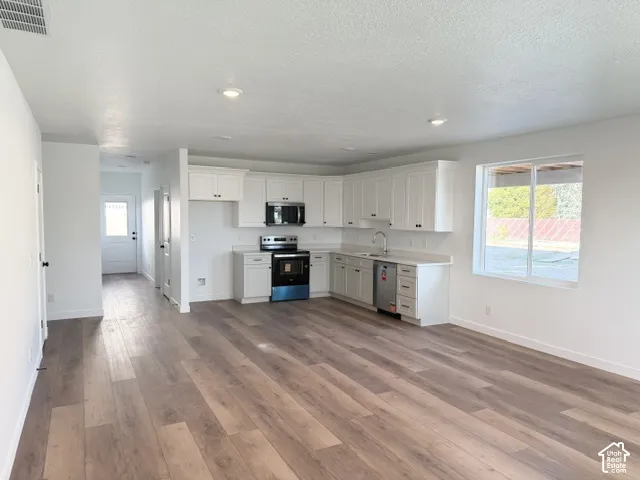 Open-concept living space featuring wood-finish flooring, recessed lighting, white cabinetry, a stainless steel appliance package, and a large window