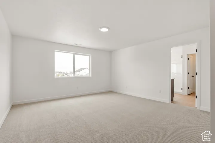 Spacious room featuring neutral carpeting, white walls, and a large window providing ample natural light