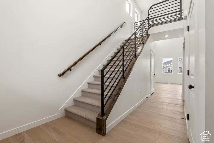 Open foyer featuring a light wood-finish flooring, a contemporary staircase with carpeted treads, dark wood-finish stringers, and a black metal railing
