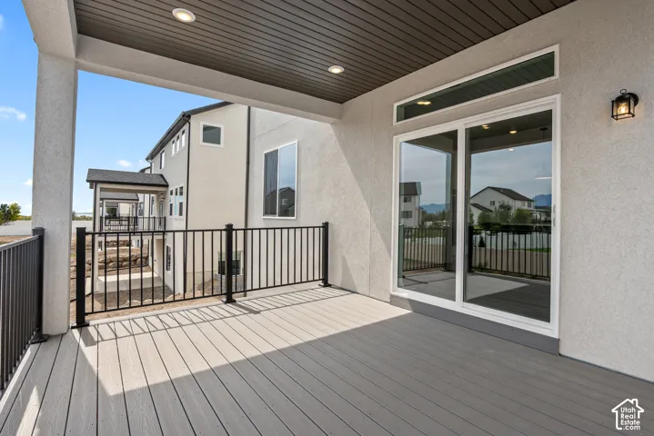 Spacious covered deck featuring composite decking, black metal railings, recessed lighting, and a large sliding glass door with a transom window