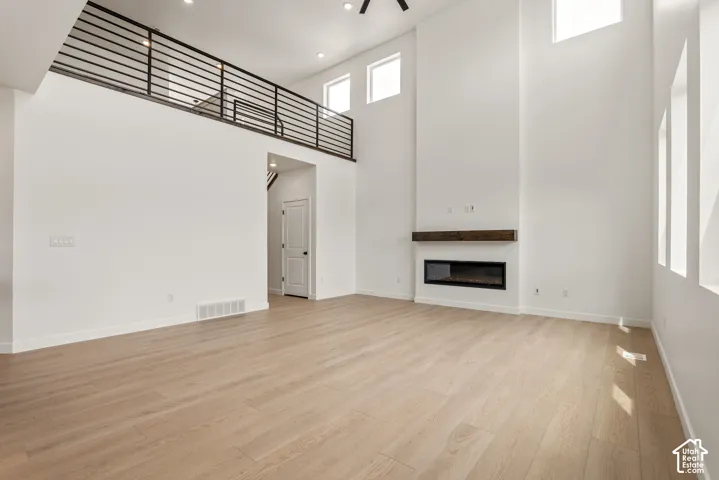 Spacious living area featuring high ceilings, wood-finish flooring, and a modern linear fireplace with a substantial wood mantel