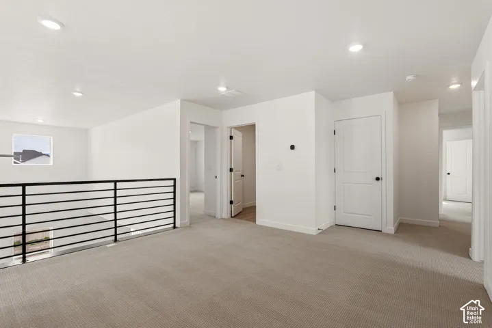 Spacious upper-level landing featuring neutral carpeting, recessed lighting, white interior doors with black hardware, and a modern black horizontal bar railing