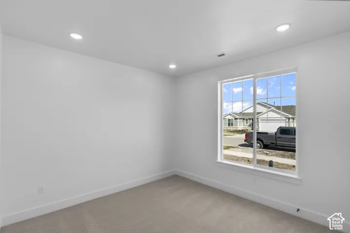 Bright room featuring a large window with grid panes, recessed ceiling lighting, light-toned carpeting, white walls, and white baseboards