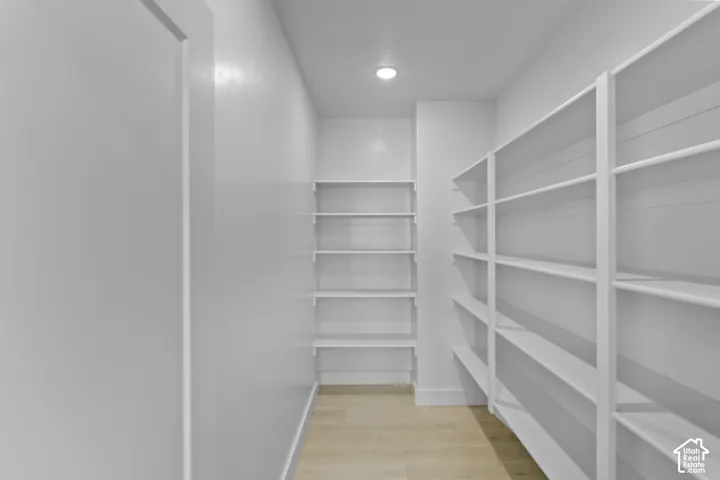 Spacious walk-in pantry featuring extensive white shelving, recessed lighting, and light wood-finish flooring