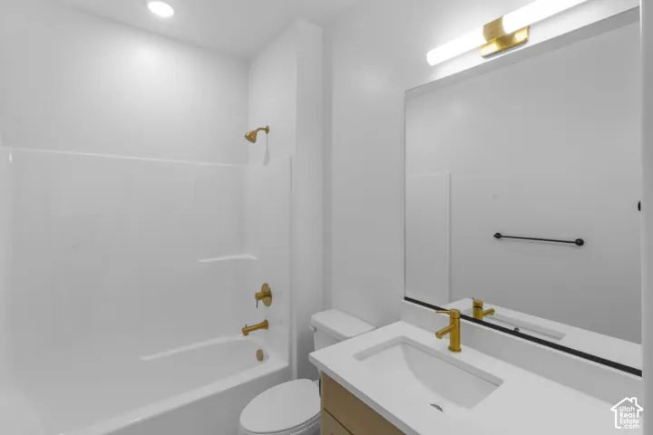 Bathroom featuring a white bathtub/shower combination, recessed ceiling lighting, a light wood-finish vanity with a white countertop, a rectangular undermount sink, and a large wall-mounted mirror with an overhead light fixture