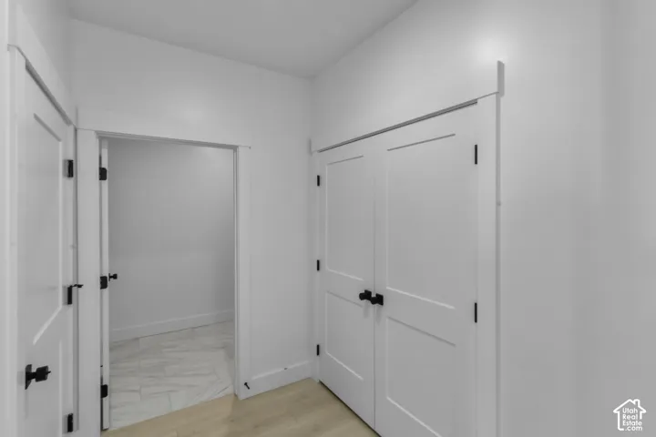Hallway featuring two-panel interior doors with matte black hardware, white baseboards, and wood-finish flooring