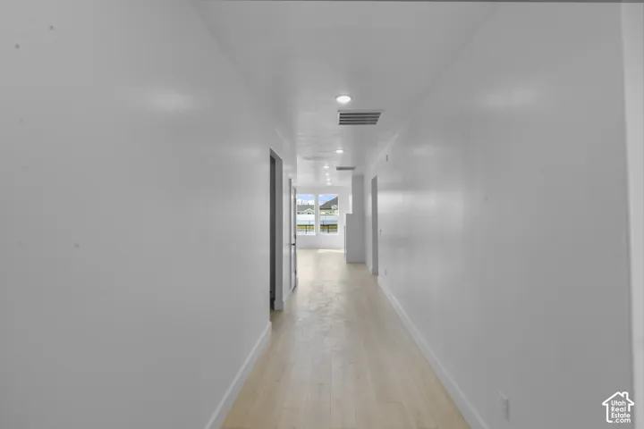 Hallway with light wood-finish flooring, recessed lighting, white walls, and distant scenery through a window