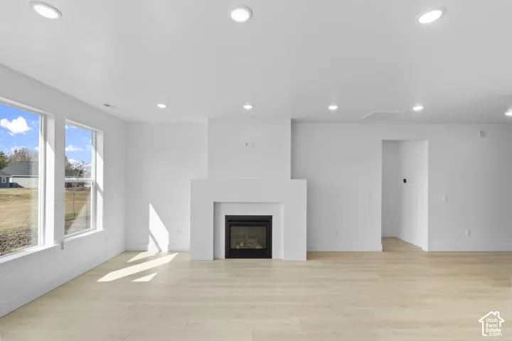 Spacious living area featuring a fireplace with a mantel, multiple large windows, wood-finish flooring, and recessed ceiling lights