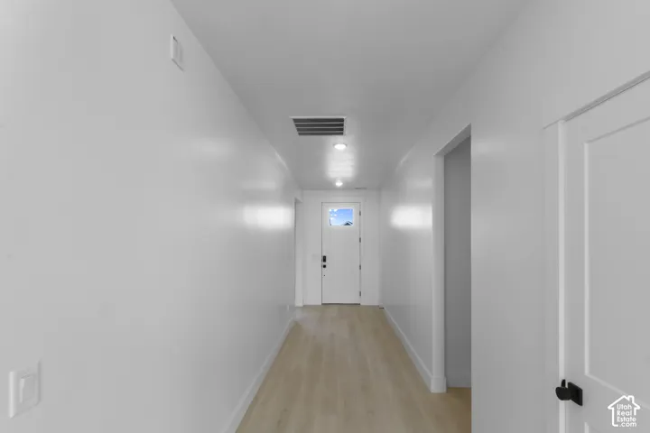 Bright hallway featuring light wood-finish flooring, recessed lighting, and a white paneled entry door with frosted glass detailing