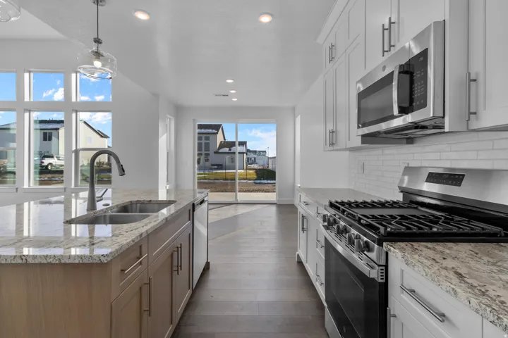 Contemporary kitchen featuring a large island with an undermount sink, granite countertops, wood-finish flooring, white shaker cabinetry, and stainless steel appliances