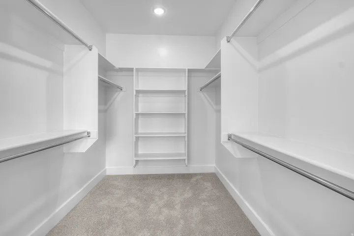Primary bedroom walk-in closet featuring white built-in shelving, white walls, light gray carpet, recessed ceiling lighting, and metal hanging rods