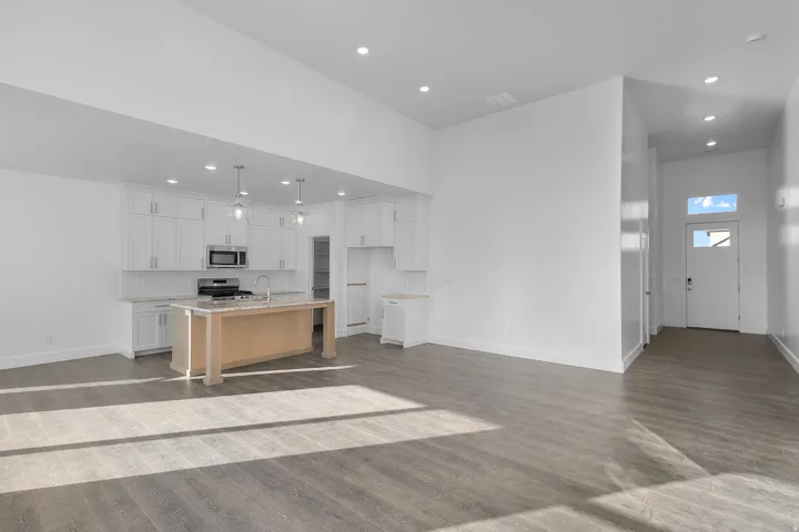 Open-concept living area featuring wood-finish flooring, a contemporary kitchen, recessed lighting, white cabinetry, and a central island with pendant lighting