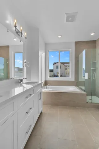 Primary bathroom featuring a dual vanity with white cabinetry and light-toned countertops, a built-in soaking tub, a separate glass-enclosed shower, and large format floor tiling