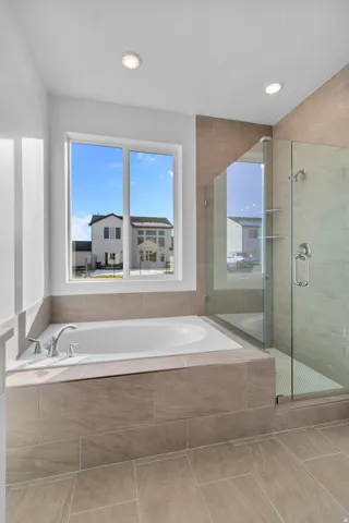 Primary bathroom featuring a built-in soaking tub with deck-mounted fixtures, a glass-enclosed shower with tile surround and recessed shelving, and large format tile flooring
