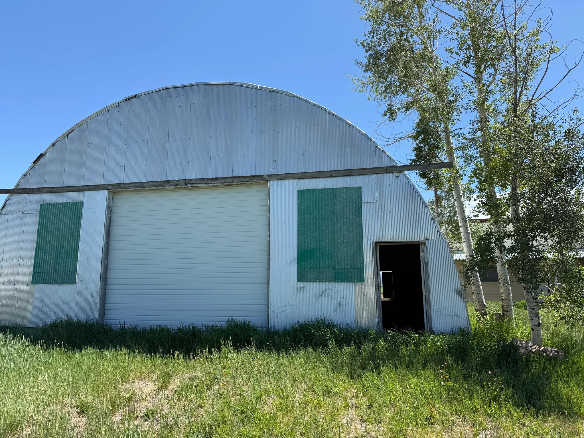 Quonset hut structure featuring corrugated metal siding, a large white roll-up door, and a standard entry door