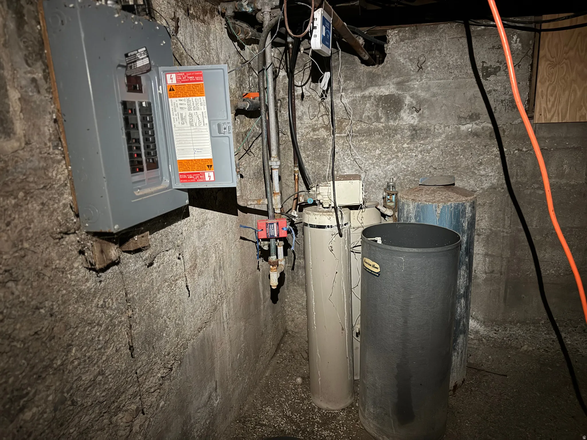 Electrical panel mounted on a textured concrete wall, alongside water heater tanks and exposed utility piping