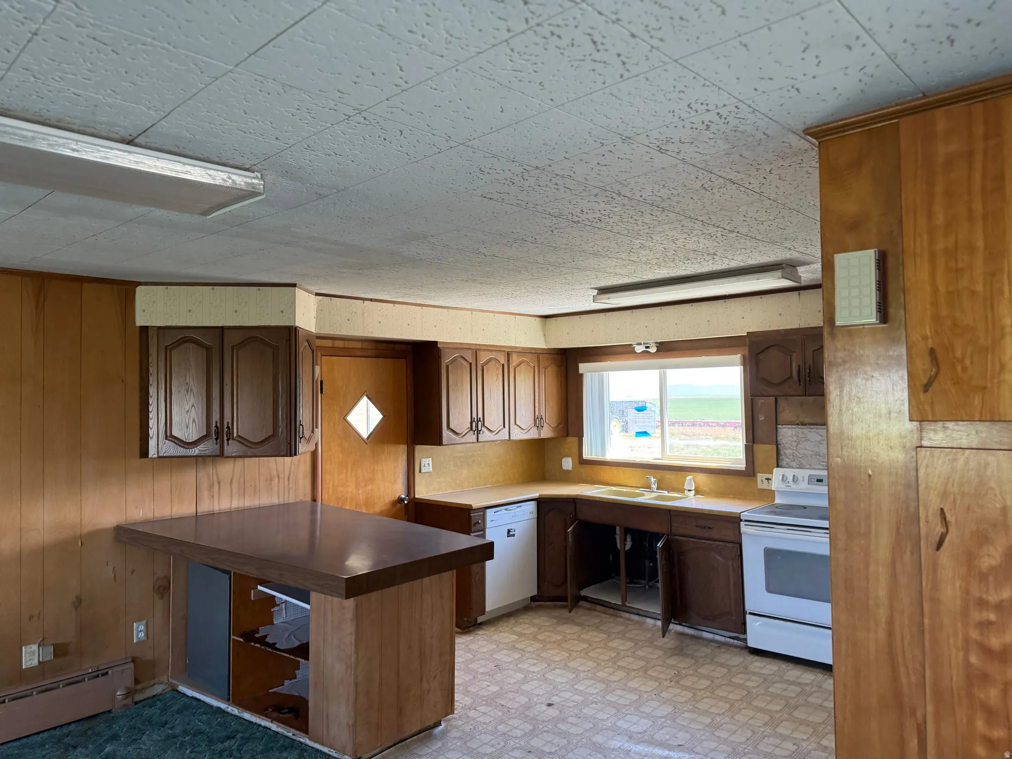 Kitchen featuring wood paneling, wood cabinetry, a built-in breakfast bar, a window above the sink, and a white electric range