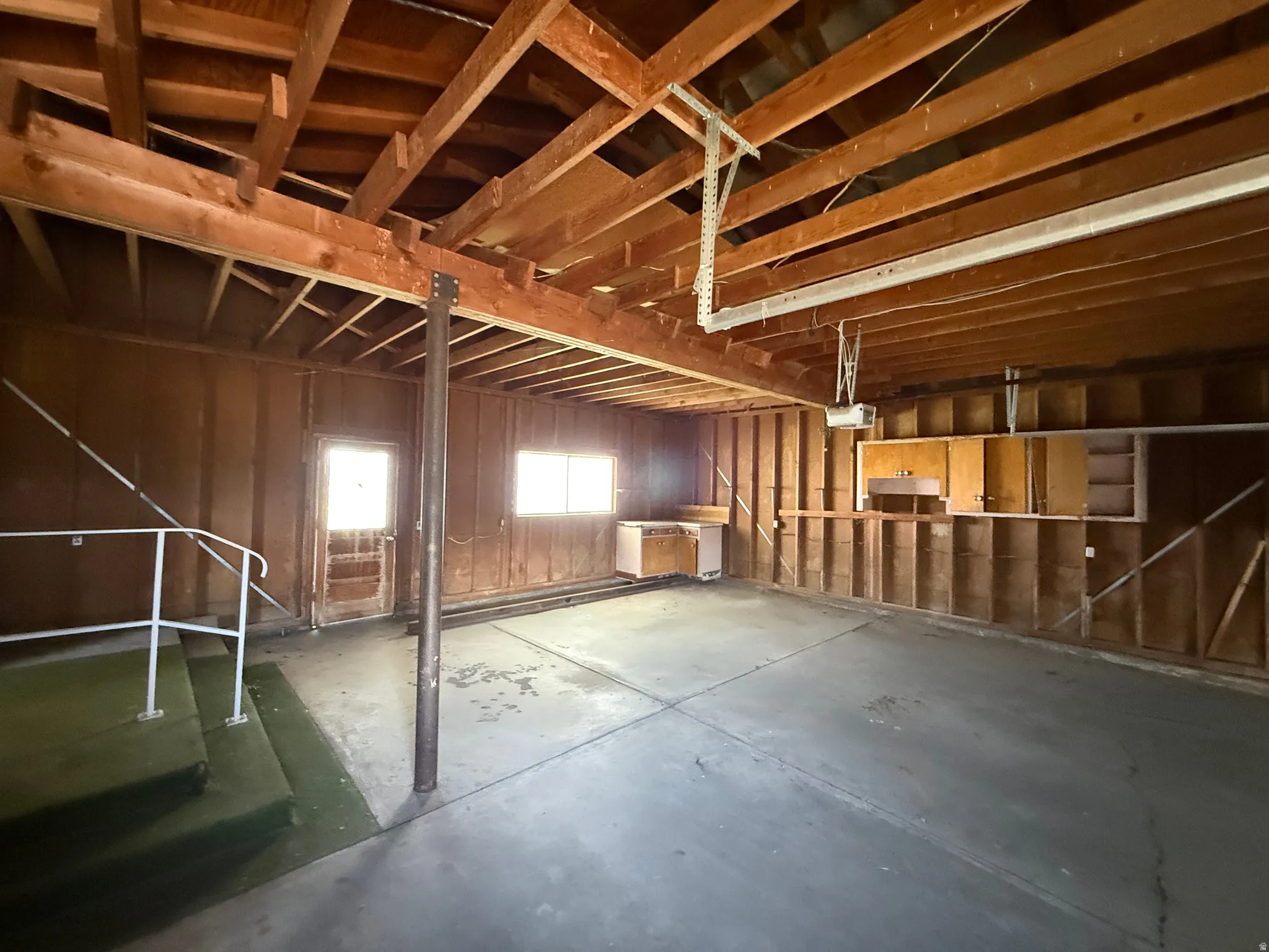 Spacious garage featuring exposed wood beam ceiling, concrete flooring, and built-in cabinetry