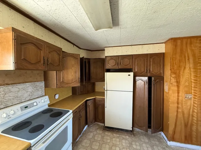 Kitchen featuring extensive wood cabinetry, L-shaped countertops, a white electric range, and a white refrigerator