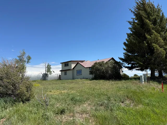 Two-story residence with light-colored siding and a reddish-brown roof, situated on a grassy landscape