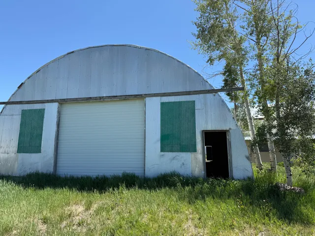 Quonset hut structure featuring corrugated metal siding, a large white roll-up door, and a standard entry door