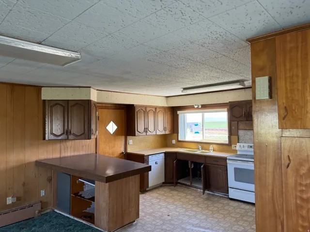Kitchen featuring wood paneling, wood cabinetry, a built-in breakfast bar, a window above the sink, and a white electric range