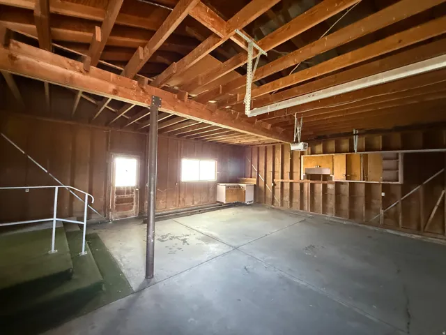 Spacious garage featuring exposed wood beam ceiling, concrete flooring, and built-in cabinetry