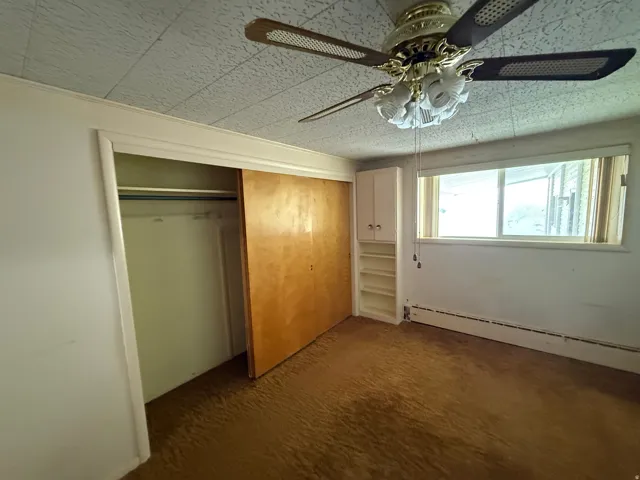 Room featuring a ceiling fan with integrated lighting, a window with horizontal blinds, and baseboard heating