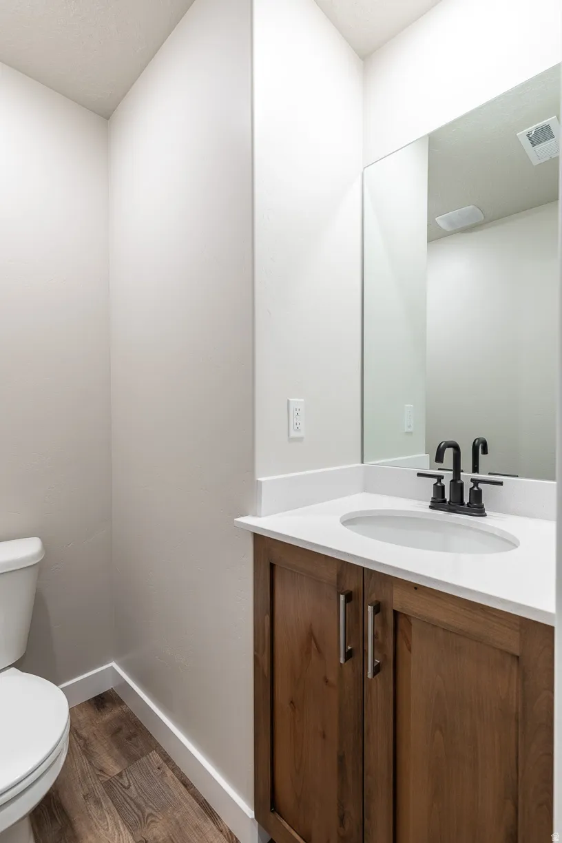 Powder room featuring a wood-finish vanity with a white countertop and undermount sink, matte black faucet, wall-mounted mirror, and wood-finish flooring